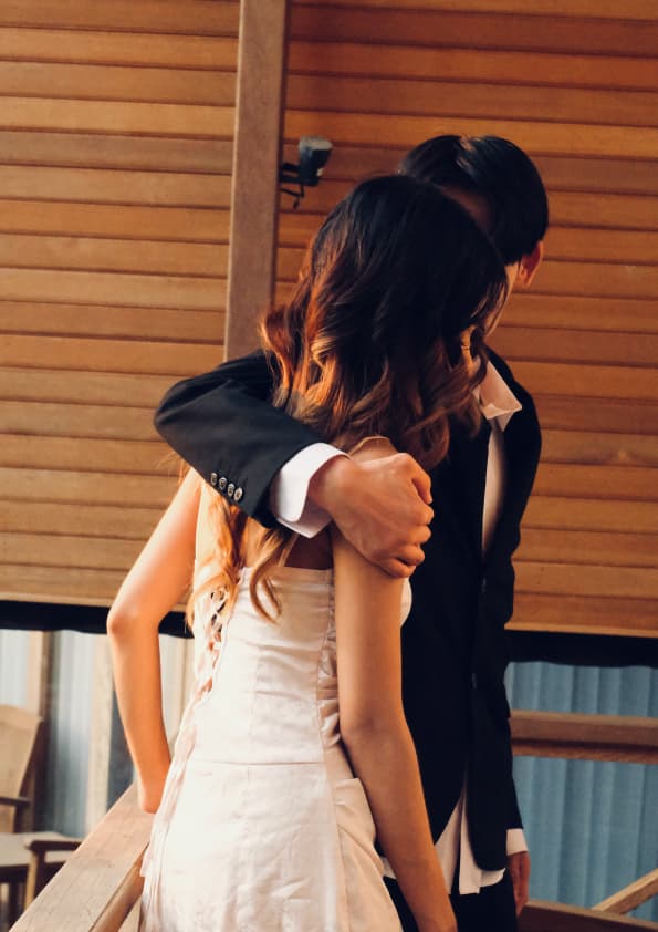 Her arms around his neck against warm wooden light