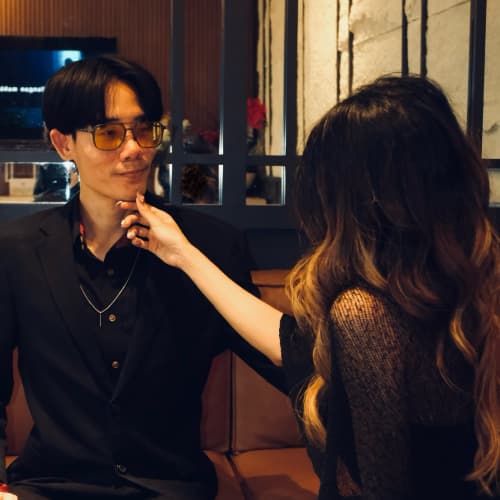 Warm restaurant light, her hand reaching for his chin